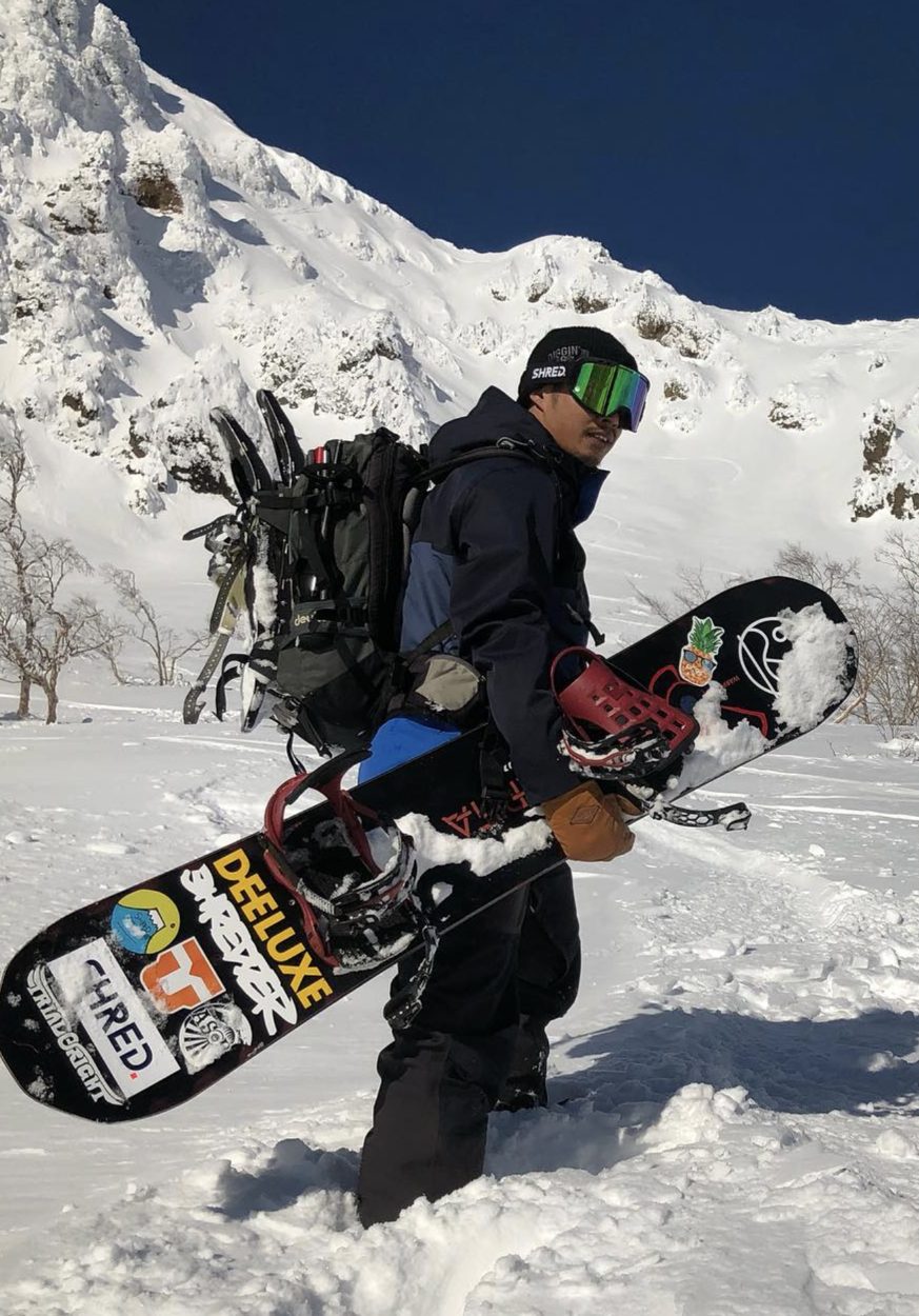平山武背著雪板站在雪山前